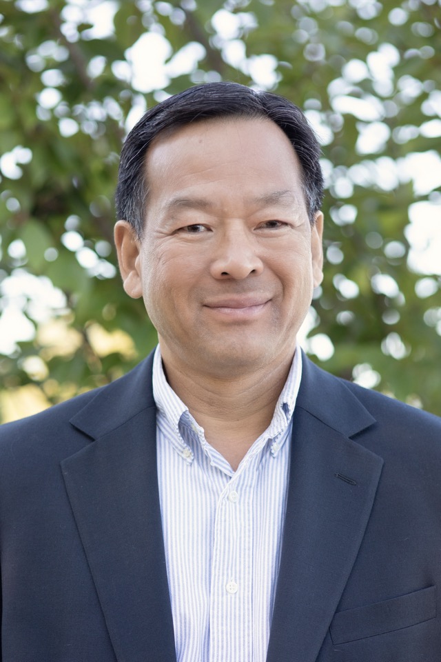 An old man wearing black color coat smiling at camera