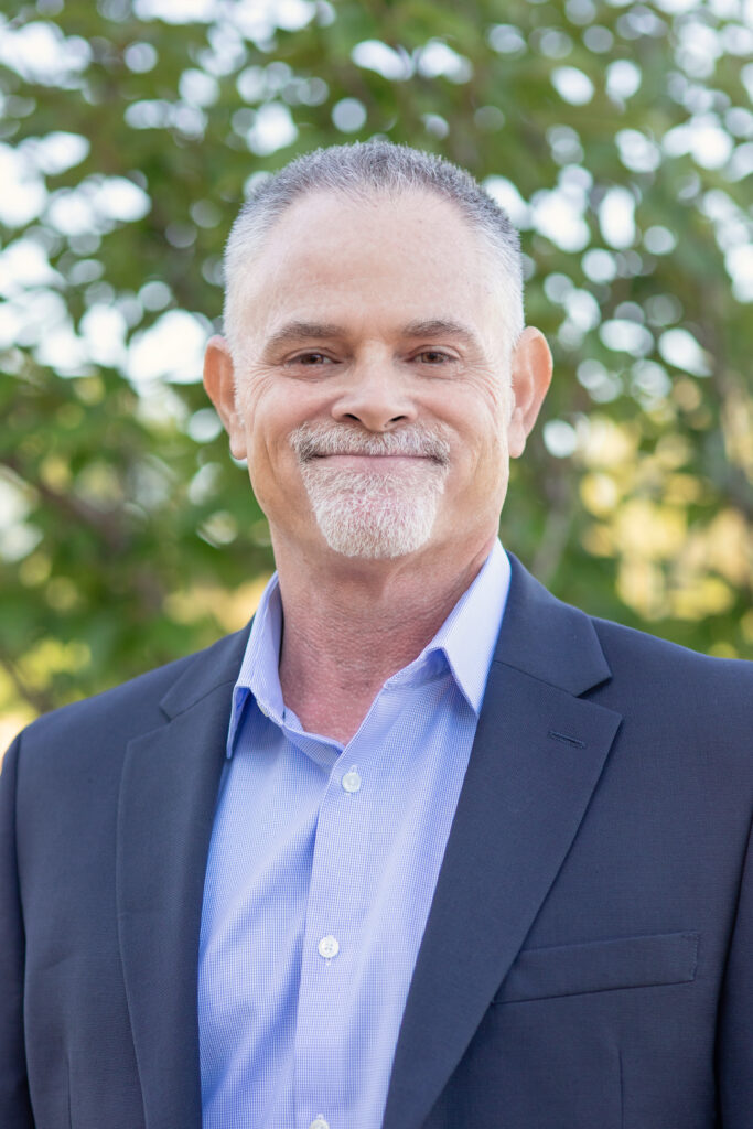 A man with white hairs and beard smiling at camera